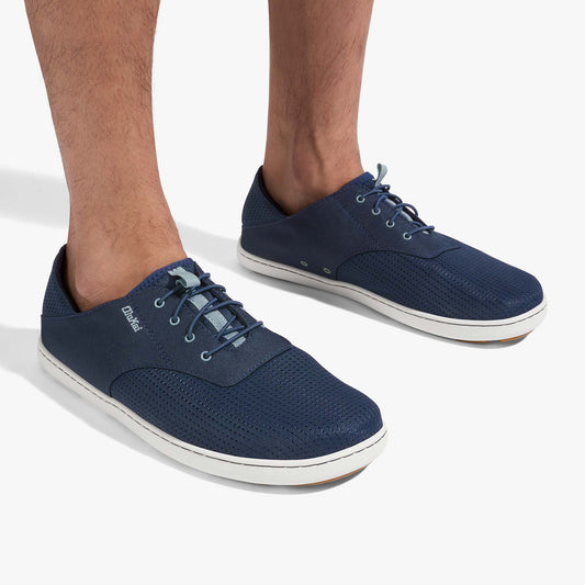 Navy blue lace-up shoes with white soles and textured fabric upper, worn on male feet.
