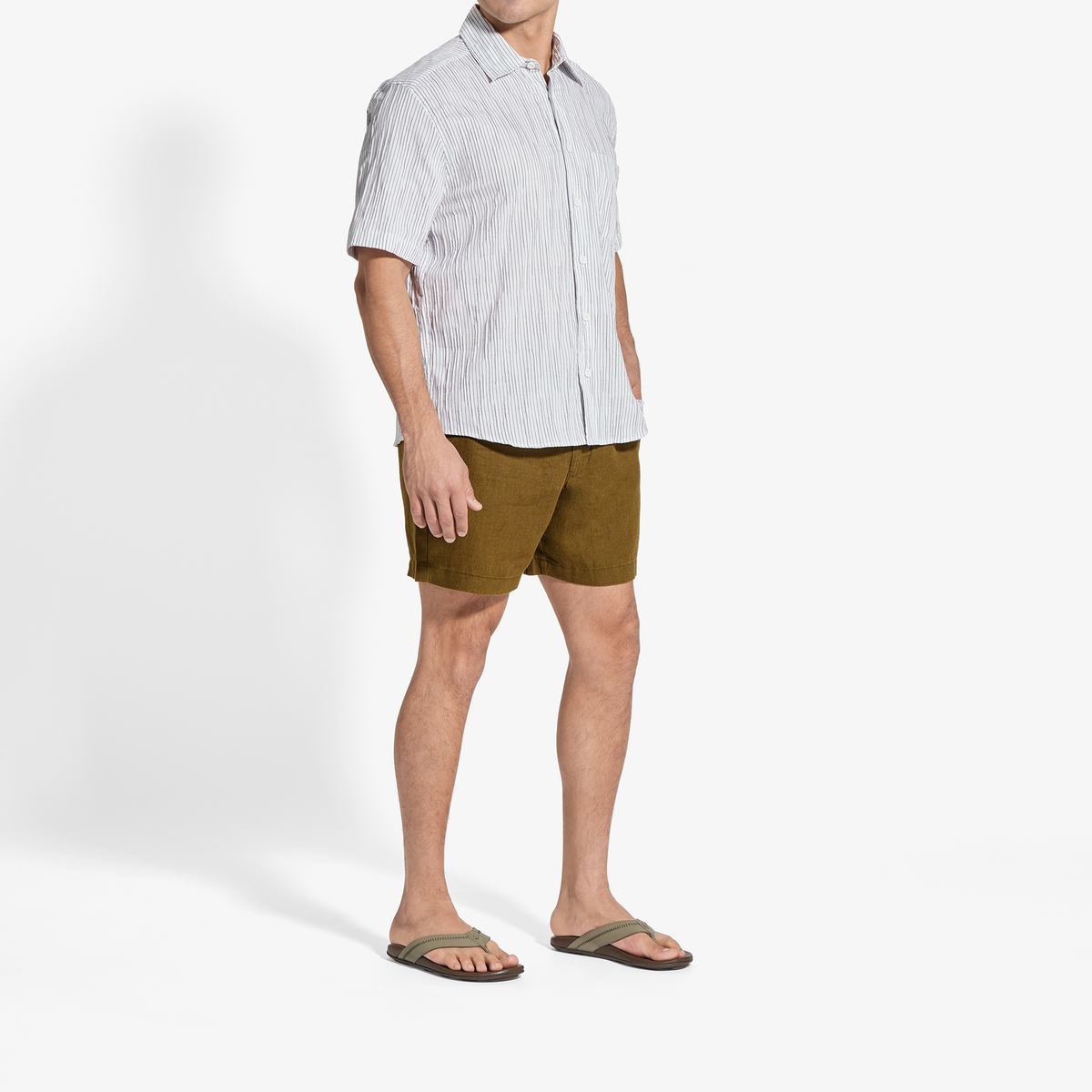 Man wearing light striped short-sleeve button-up shirt and olive green shorts with sandals.