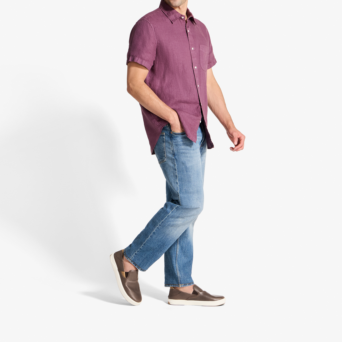 Man wearing a burgundy short-sleeve button-up shirt with blue jeans and brown slip-on shoes.