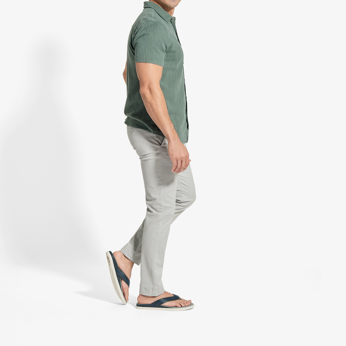 Man wearing sage green short-sleeve button-up shirt and pale grey pants with dark slide sandals.