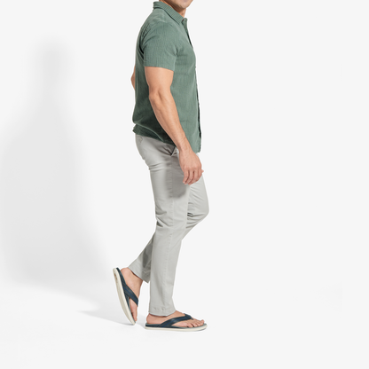 Man wearing sage green short-sleeve button-up shirt and pale grey pants with dark slide sandals.