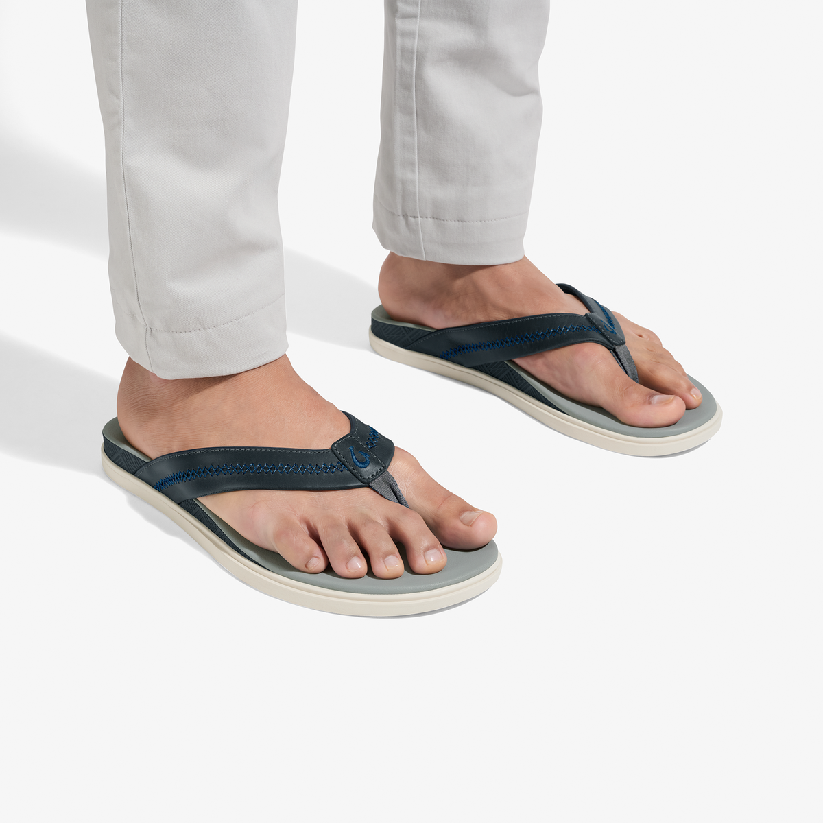 Person wearing pale grey pants and navy thong sandals with grey and cream soles.