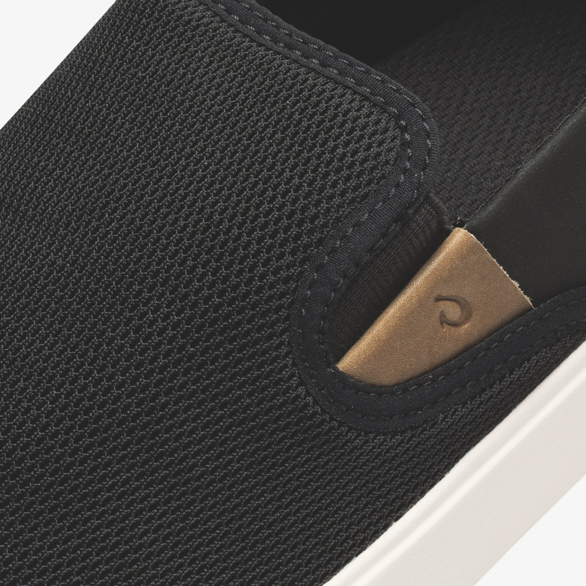 Black textured slip-on shoe with tan leather heel patch and white sole detail.