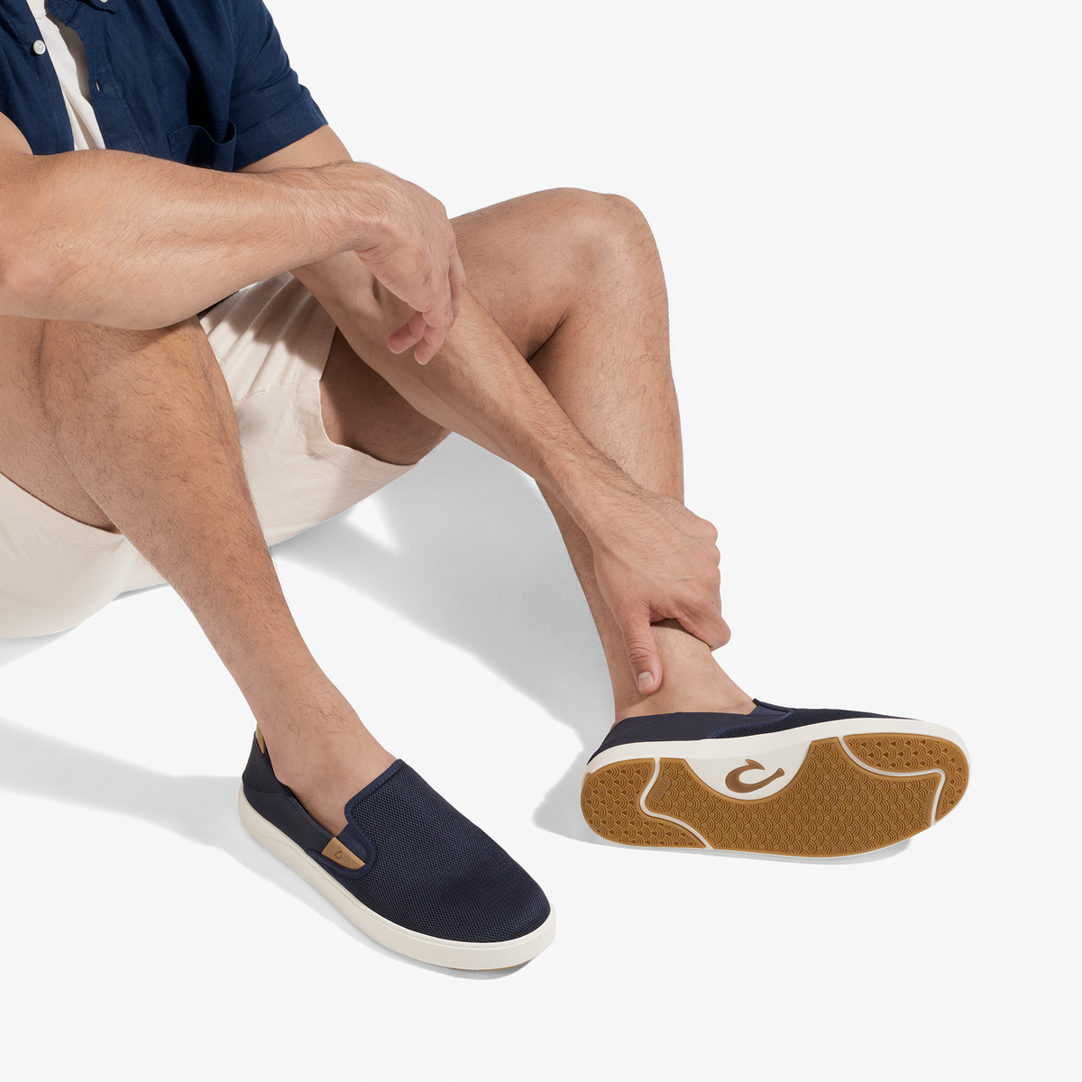 Man wearing navy slip-on sneaker with cream sole and tan/brown gum rubber outsole, paired with white shorts and navy shirt.