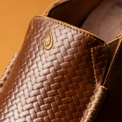 Toffee-colored woven lauhala bag with gold embroidered hook detail on front panel and dark java lining visible inside.
