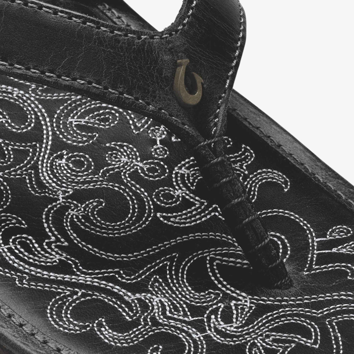 Black leather bag with white embroidered scrollwork design and metal D-ring hardware detail.
