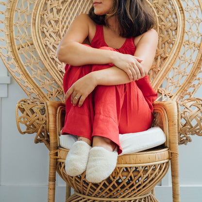 Cream-colored wool mule slipper with rounded toe on model's foot.
