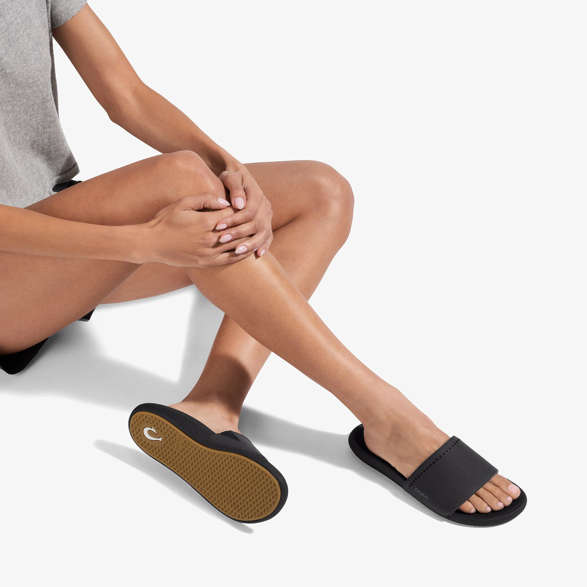 Black slide sandal with textured brown sole, worn on foot against white background.