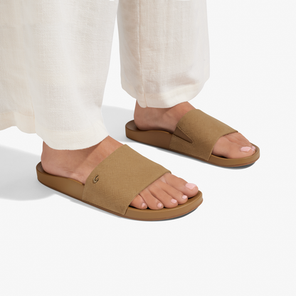 Tan crosshatch slide sandals with brown soles worn with cream pants.