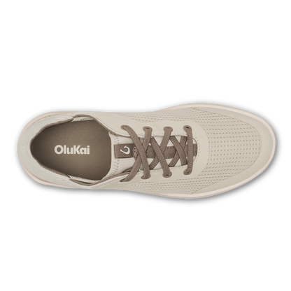 Cream-colored OluKai sneaker with perforated upper, brown laces, and visible brand logo on tongue, shown from above.